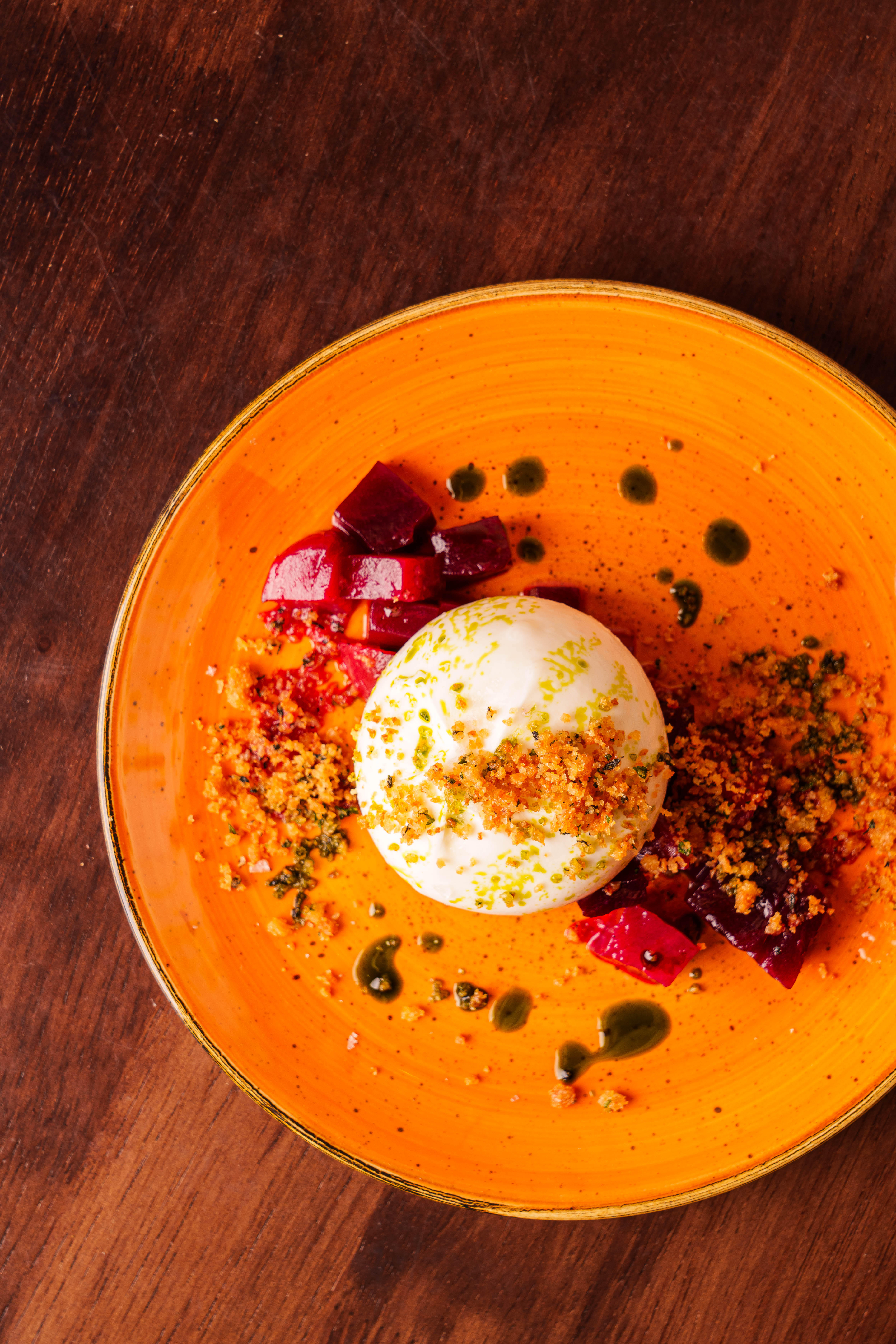 Burrata with roasted beets and breadcrumbs on an orange plate.